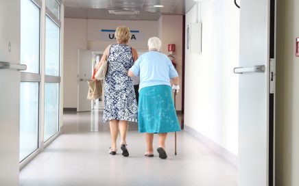 Elderly woman and younger woman walking along a hospital corridor