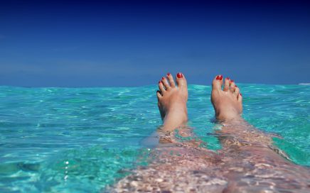 Person lying in crystal clear water-toenails painted red