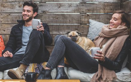 Happy couple-pug-drinking from mugs-wooden house
